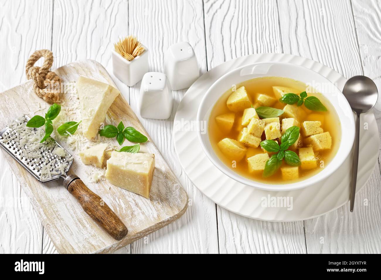 Zuppa imperiale, italienische Suppe aus Hühnerbrühe mit Parmesan-Eierknödeln, bestreut mit geriebenem Käse und Basilikum in einer Schüssel auf einem Holztisch Stockfoto