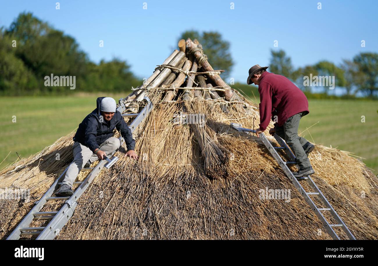 Veteran Jesse Swanson (links) schließt sich will Scanlan der Butser Ancient Farm an, als sie das Dach eines neuen bronzezeitalten Rundhauses auf der Butser Ancient Farm in Hampshire umhauen. Das Rundhaus, das an diesem Wochenende der Öffentlichkeit vorgestellt wurde, wurde von Veteranen der Operation Nightingale errichtet, einer Initiative, die die Wiedergewinnung von Militärs und Veteranen durch die Einbeziehung in die Archäologie, Und nahm mehr als 1000 Stunden ehrenamtlicher Arbeit zu bauen und ist das erste Rundhaus aus der Bronzezeit auf dem Gelände, das Häuser von der Steinzeit bis zum angelsächsischen umfasst. Bilddatum: Mittwoch, 6. Oktober 2021. Stockfoto