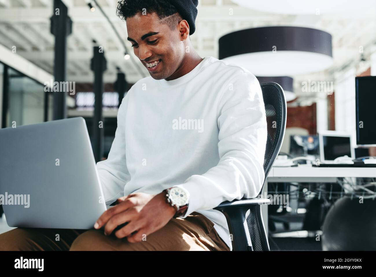 Lächelnder Geschäftsmann, der in einem modernen Büro an einem Laptop arbeitet. Glücklicher junger Geschäftsmann, der gerne allein an einem modernen Arbeitsplatz arbeitet. Kreative junge Busin Stockfoto