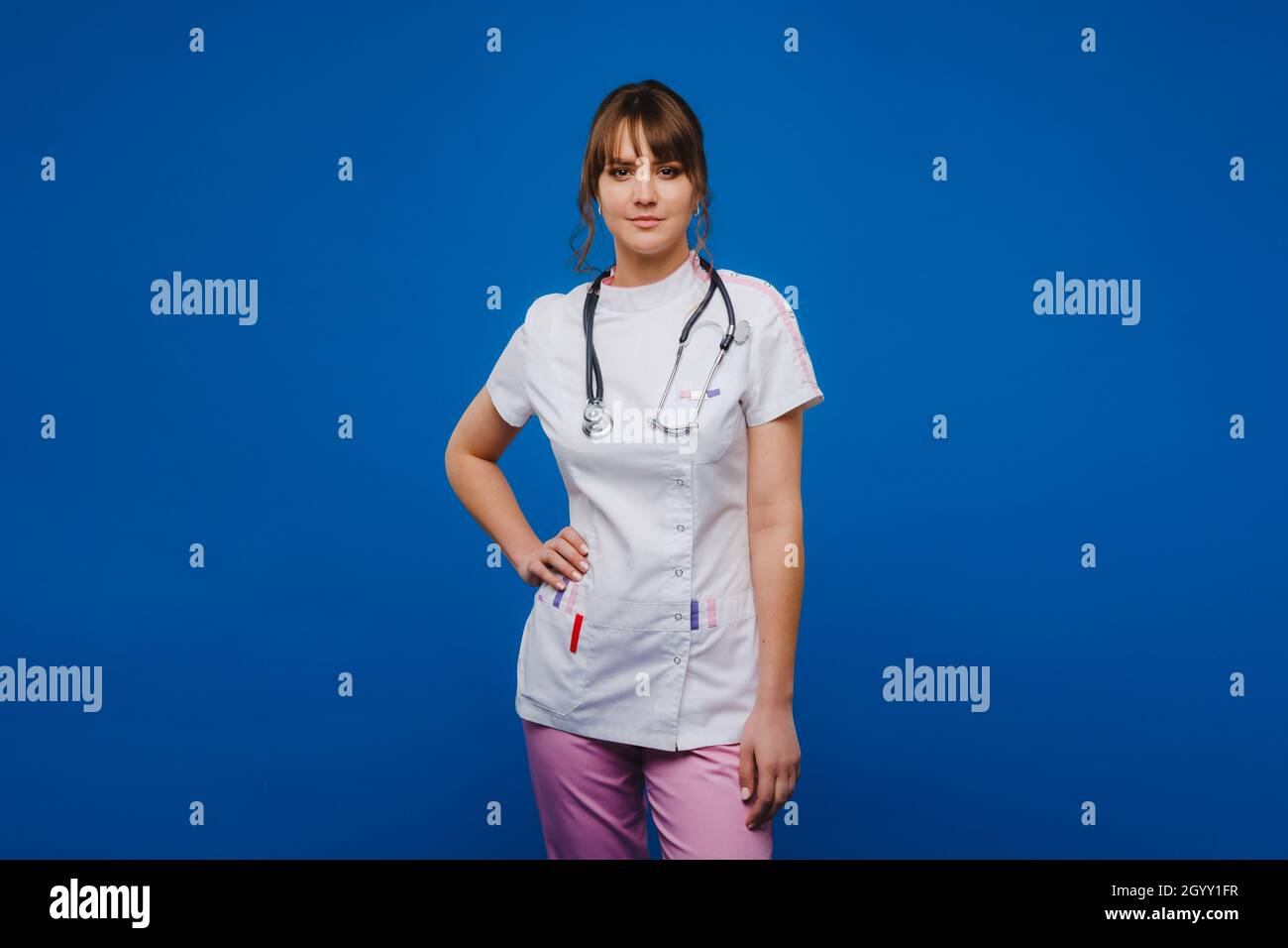 Eine gestikulierende Ärztin überprüft den Herzschlag in der Arztpraxis des Krankenhauses mit einem Stethoskop, das auf blauem Hintergrund isoliert ist. Stockfoto