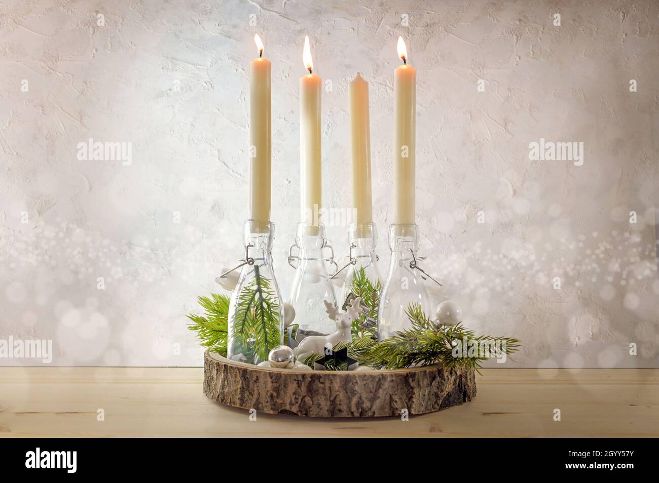 Kreativer Adventskranz, Kerzen in Flaschen auf einem Holzbrett mit Tannenzweigen und Dekoration an einer hellen rustikalen Wand, drei werden am dritten angezündet Stockfoto