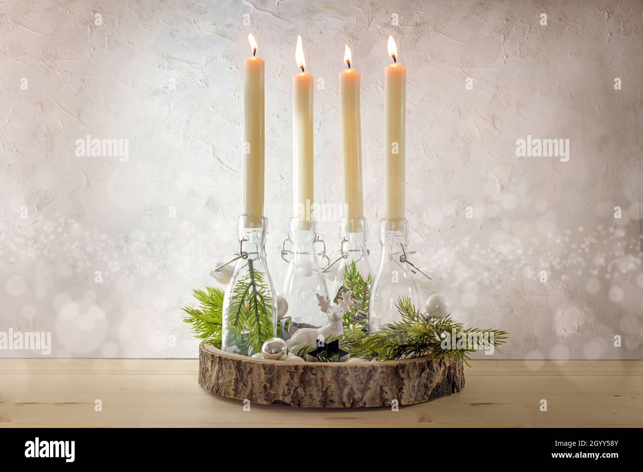 Kreativer Adventskranz, vier brennende Kerzen in Flaschen auf einem Holzbrett mit Tannenzweigen und Dekoration an einer leichten rustikalen Wand am vierten Sunda Stockfoto