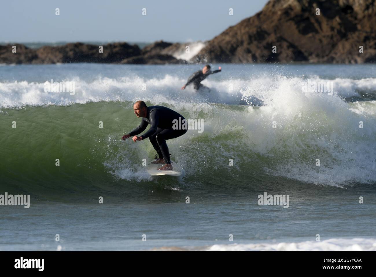 Beim Surfen an einer der vielen geschützten Buchten von Gower „tuckt“ sich ein Surfer, der sich für eine Schlauchwelle anlegt Stockfoto