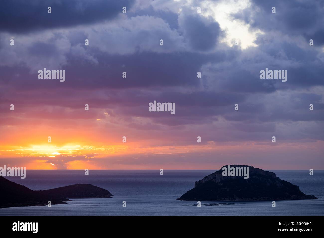 Atemberaubender Sonnenaufgang an einem bewölkten Tag mit einer Küste und der Insel Figarolo, die von einem ruhigen Wasser gebadet ist. Golfo Aranci, Sardinien, Italien. Stockfoto