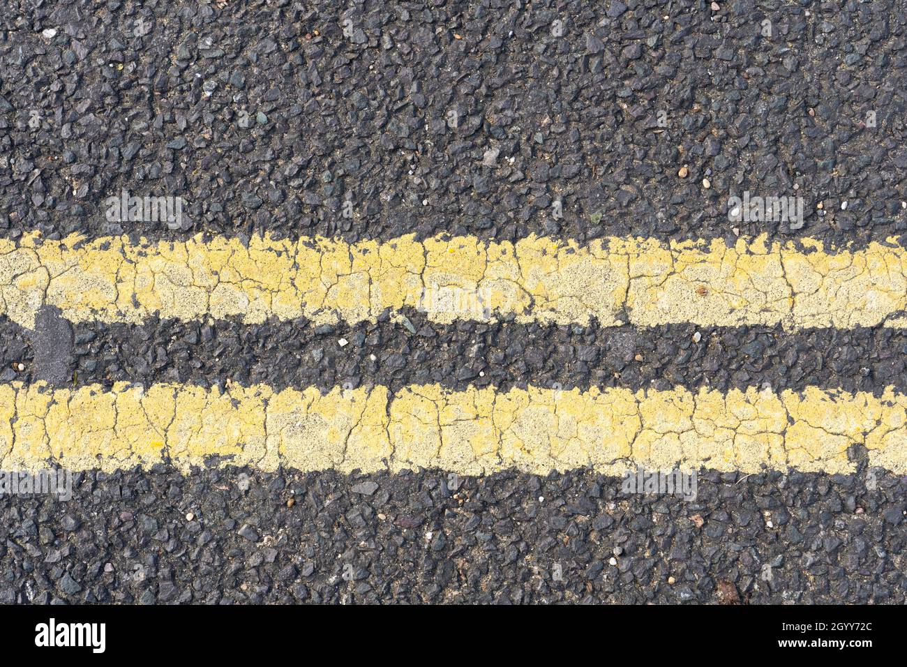 Doppelte gelbe Linien in thermoplastischer Farbe auf einer Asphaltstraße in England, die das Parken und Warten zu jeder Zeit verbieten Stockfoto