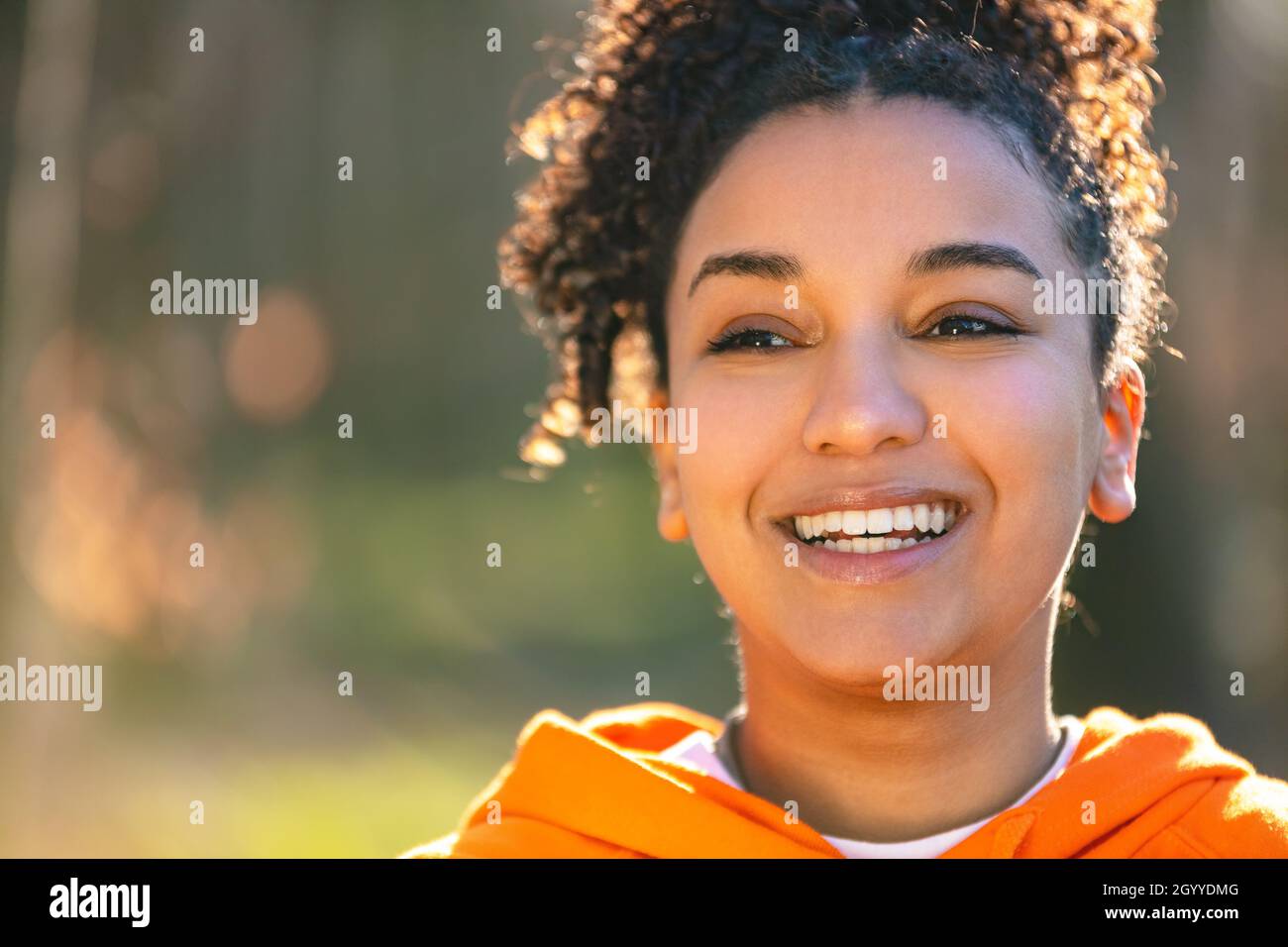 Outdoor-Porträt von schönen glücklich gemischt Rasse biracial afroamerikanischen Mädchen Teenager weibliche junge Frau lächeln mit perfekten Zähnen trägt eine Orange Stockfoto