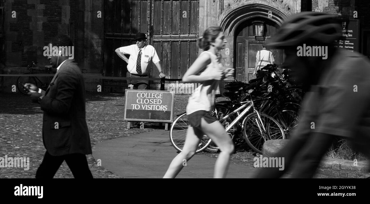 Ein College-Portier, außerhalb des Trinity College, Cambridge, lehnt sich an einen Posten und beobachtet die Welt an sich vorbei. Stockfoto