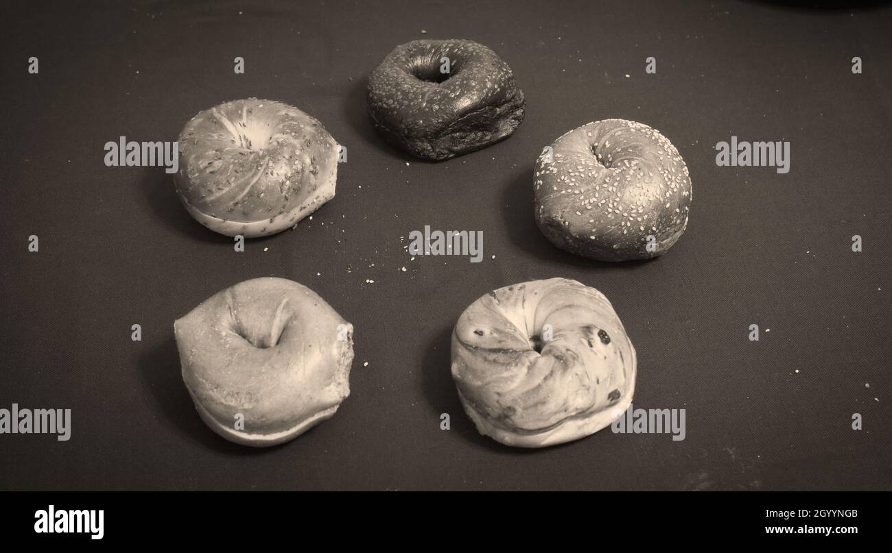 Fünf Bagels, jeweils mit einzigartigen Mischungen, in einem Kreis auf dunklem Hintergrund angeordnet Stockfoto