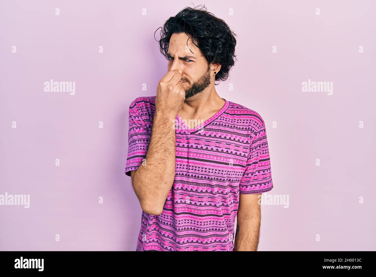 Hübscher hispanischer Mann in einem lässigen rosa TShirt, der etwas stinkendes und ekelhaftes