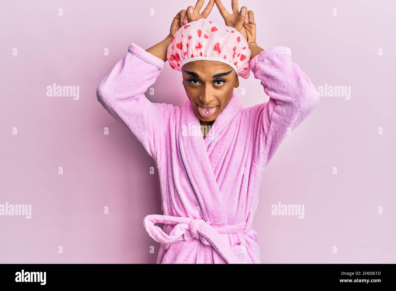 Hispanic Mann trägt Make-up mit Duschhandtuchkappe und Bademantel posiert  lustig und verrückt mit den Fingern auf dem Kopf als Hasenohren, lächelnd  fröhlich Stockfotografie - Alamy