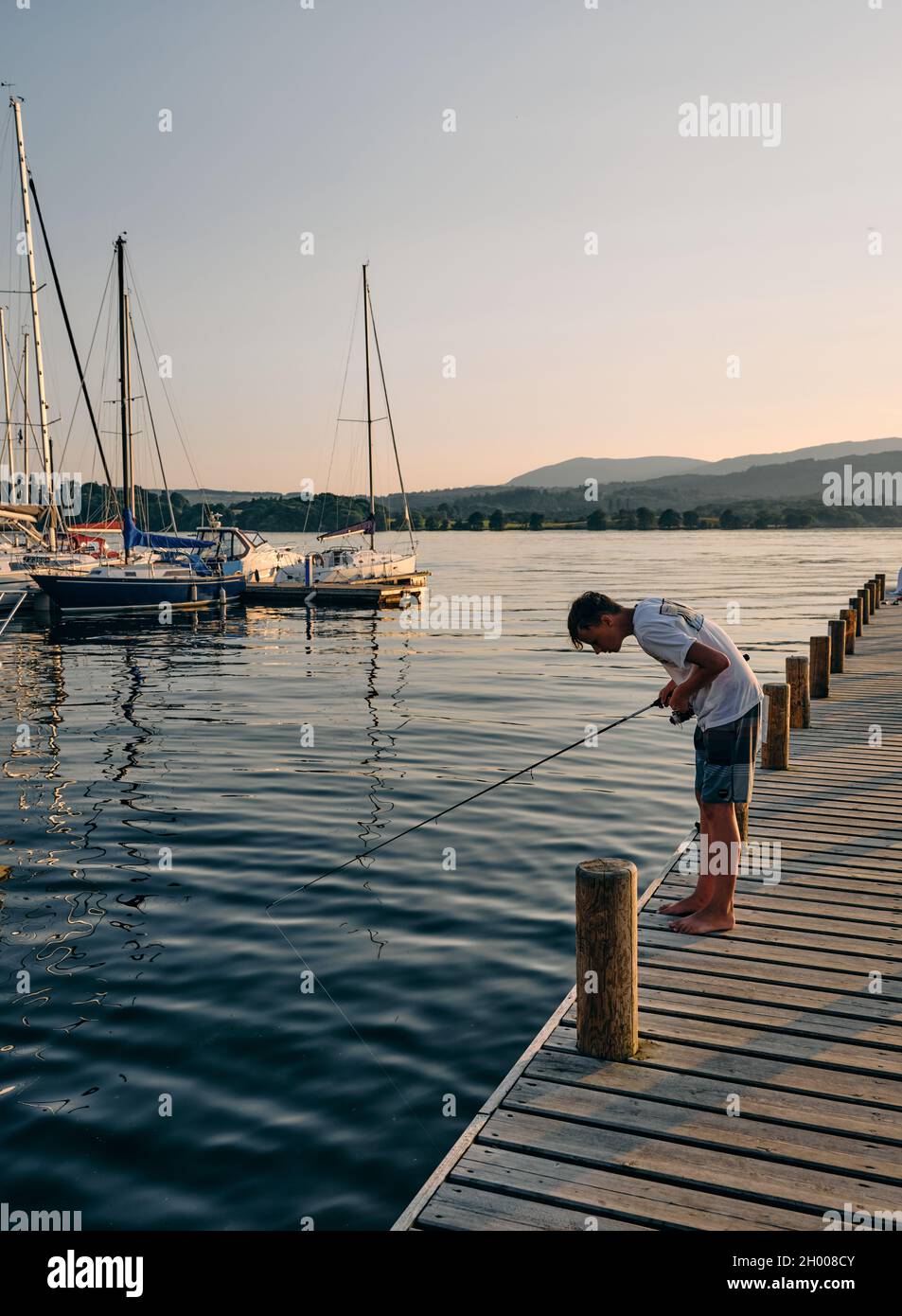 Angeln von einem Ponton auf dem Lake Windermere und den fernen Langdales in der Low Wood Bay bei Sonnenuntergang im Lake District Cumbria England Stockfoto