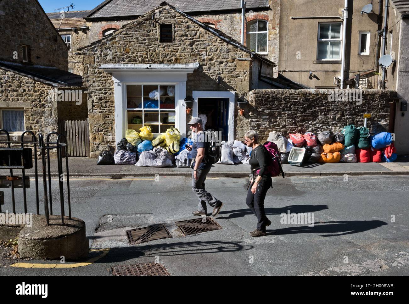 Spaziergänger passen vor dem Waschsalon in der Stadt Settle in Yorkshire Dales, North Yorkshire, Großbritannien, Taschen mit Kleidungsstücken, einige davon aus Ferienunterkünften Stockfoto