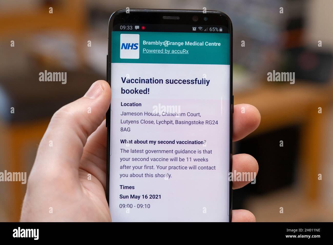 Eine Buchung für eine Covid-19 Coronavirus-Impfung in England wird auf der NHS-App auf einem in der Hand eines Mannes gehaltenen Smartphone-Bildschirm angezeigt Stockfoto