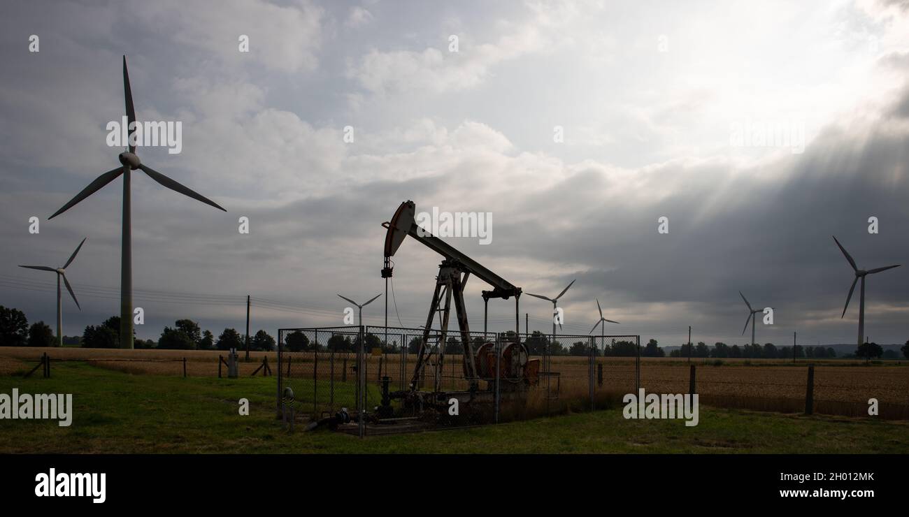 Alte rostige Ölfördermaschinen vor modernen Windkraftanlagen, die die Energiewende angesichts des Klimawandels symbolisieren Stockfoto