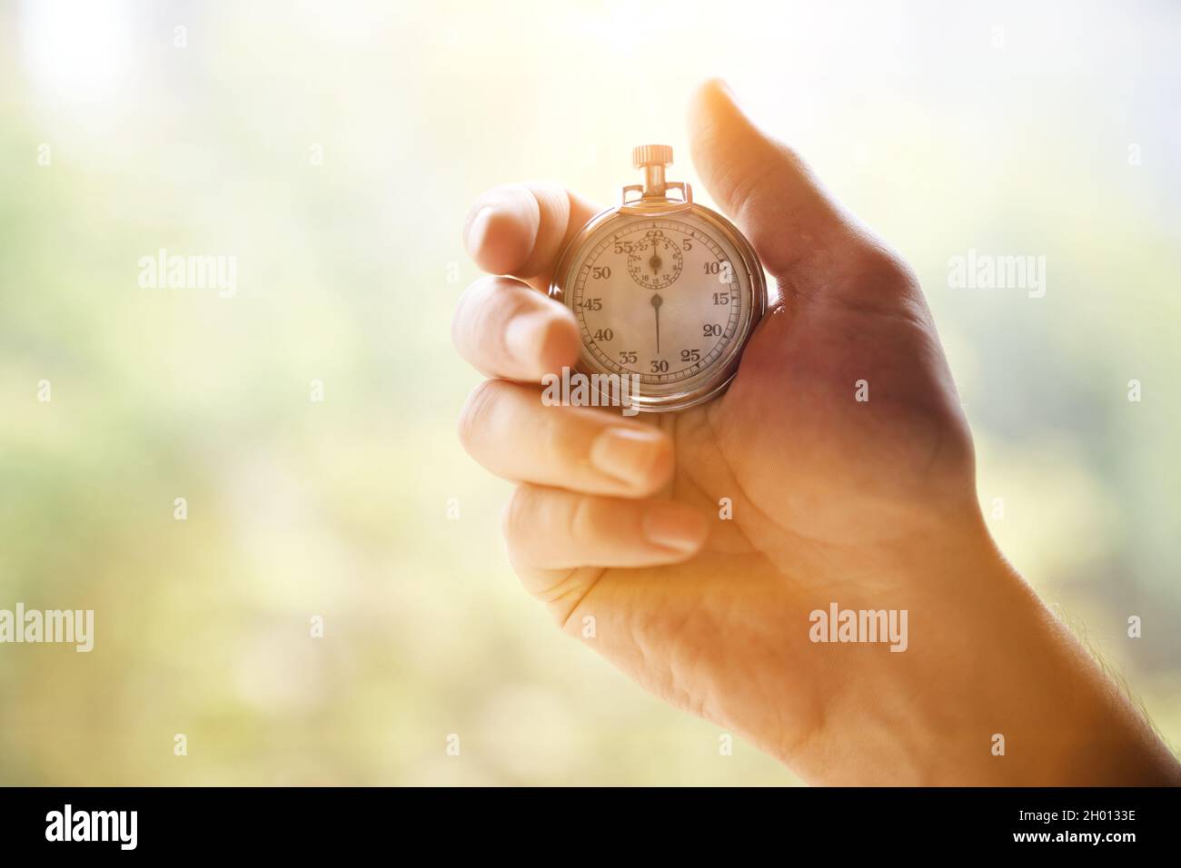 Eine Männerhand hält eine klassische mechanische Metallchrom-Stoppuhr auf einem unfokussiertem grünen Hintergrund. Hochwertige Fotos Stockfoto