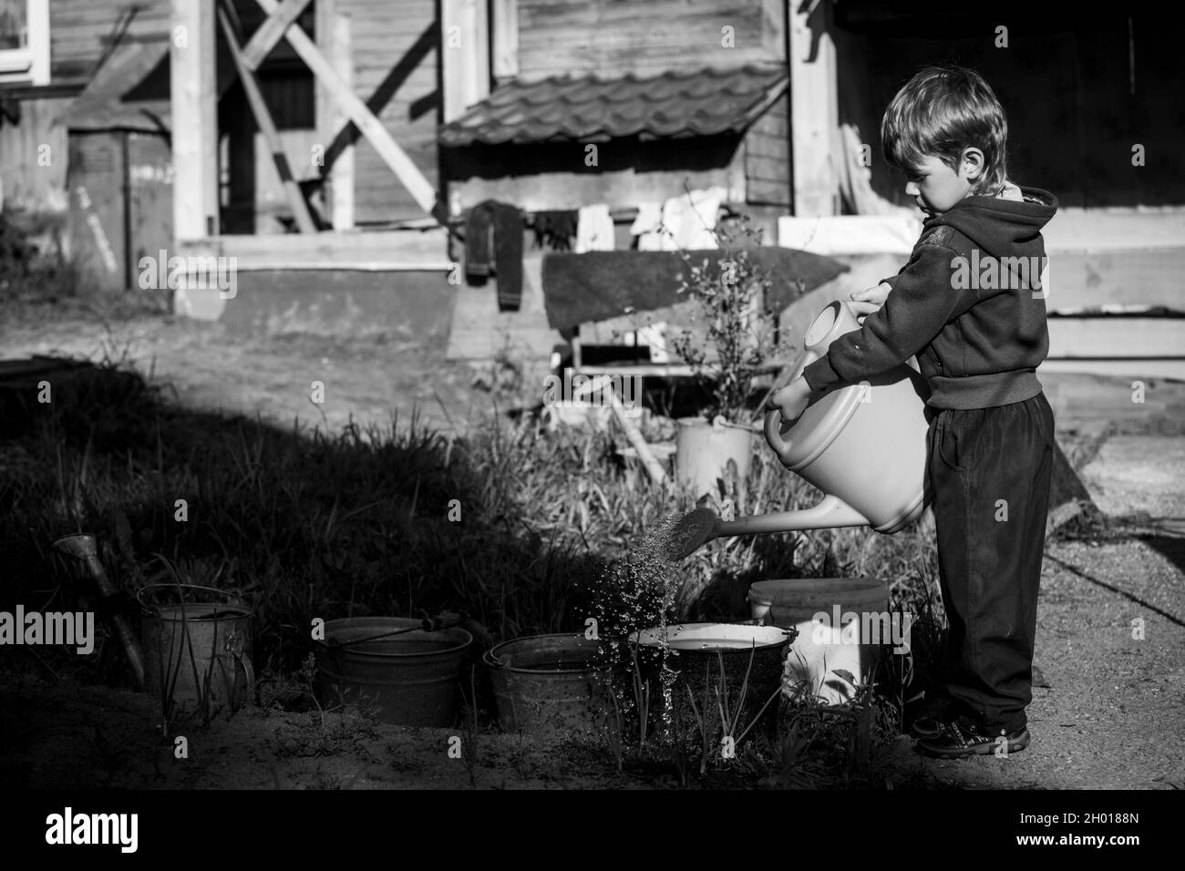 Ein kleiner Junge wässert die Betten im Dorf mit einer Gießkannen. Schwarzweiß-Foto. Stockfoto