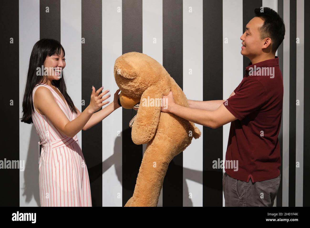 Die junge asiatische Frau erhält von ihrem Freund in einem gestreiften Zimmer einen Teddybär. Stockfoto