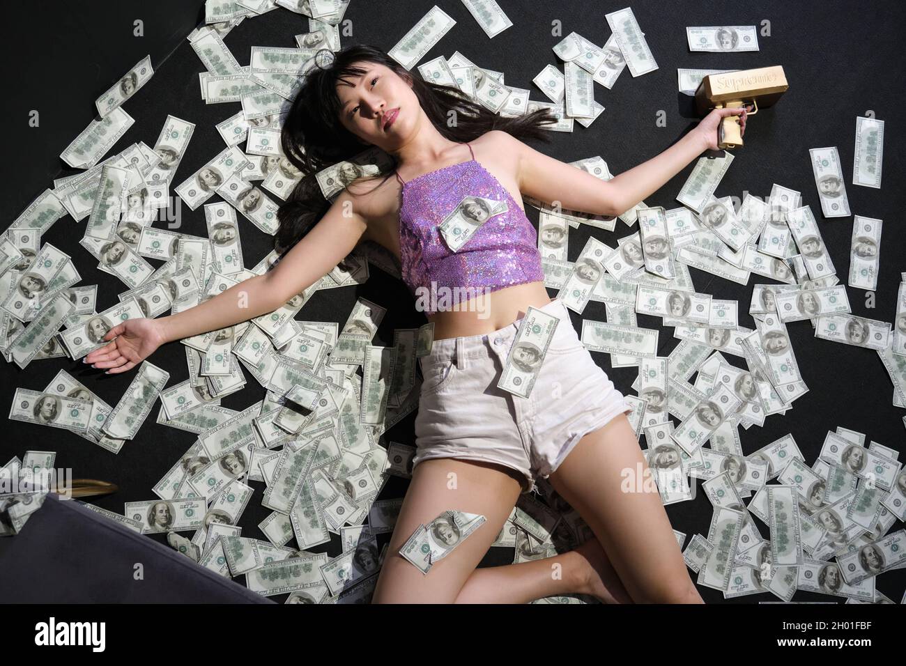 Verstorbene junge asiatische Frau, umgeben von Dollarscheinen. Selbstmord mit einem Schuss. Stockfoto