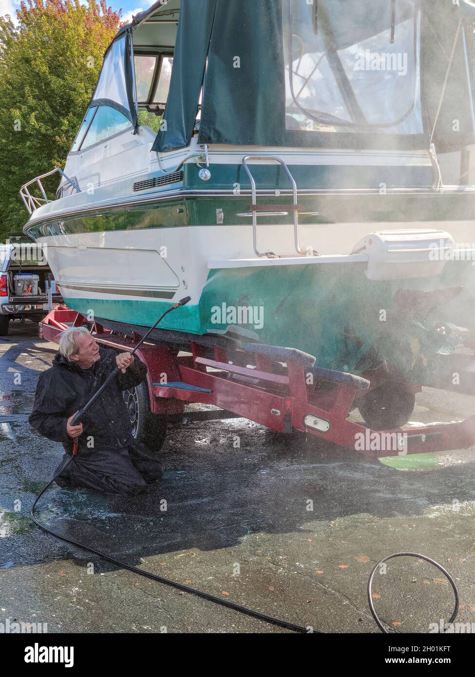 Kaukasischer Mann trägt einen schwarzen wasserdichten Anzug, während er das Motorboot druckwascht Stockfoto