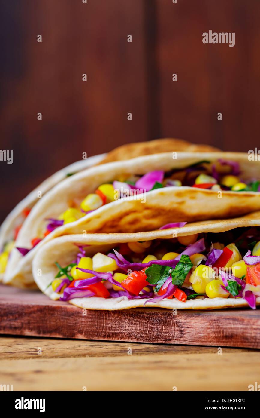 Vegane Tacos mit verschiedenem Gemüse auf einem Schneidebrett. Tacos mit süßem Mais, purpurem Kohl und Tomaten auf Holzbrettern. Speicherplatz kopieren Stockfoto