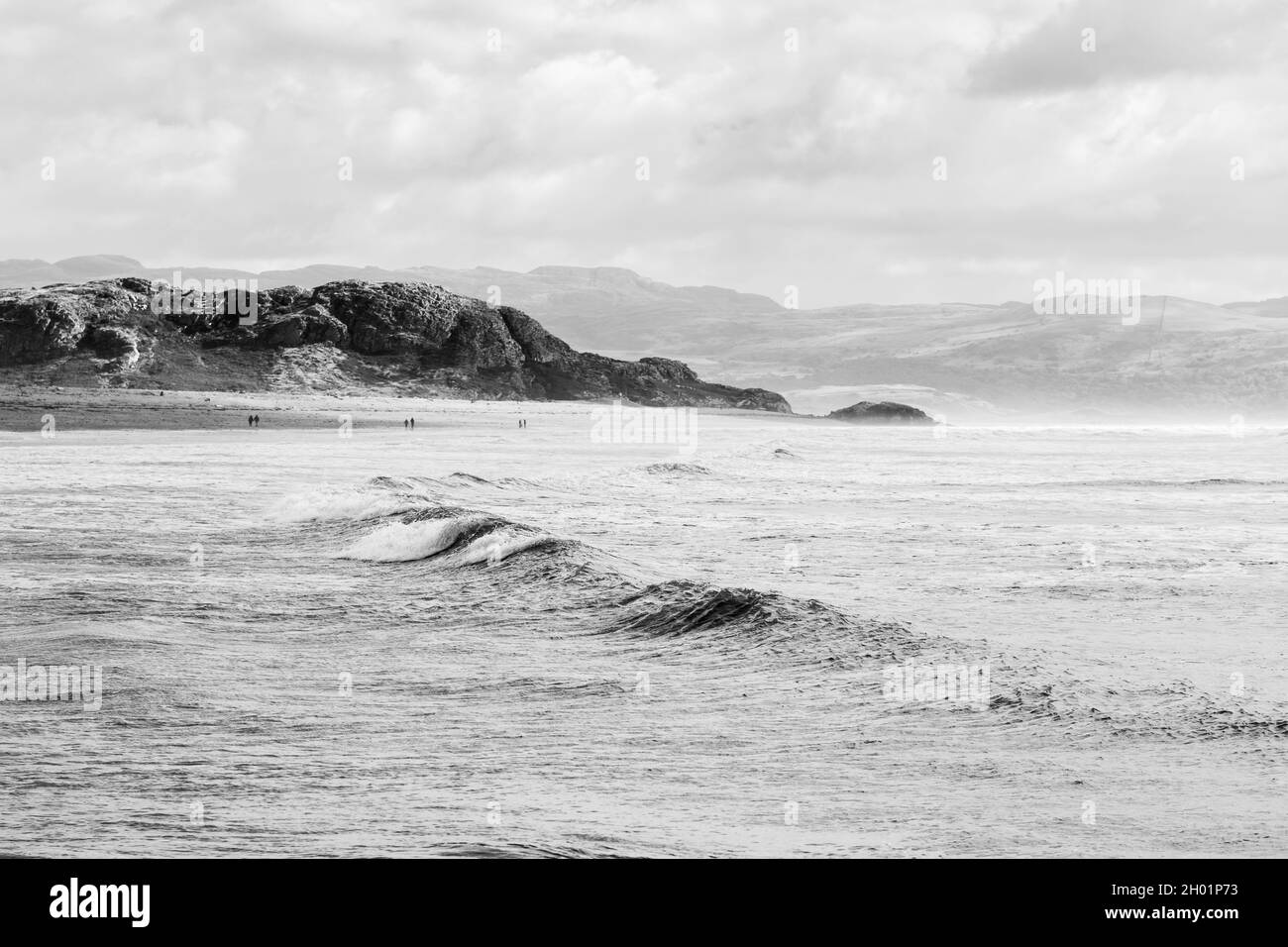 Wellen stürzen auf den Strand von Criccieth an der Küste von Nord-Wales, während die Berge von Snowdonia den Hintergrund säumen. Stockfoto