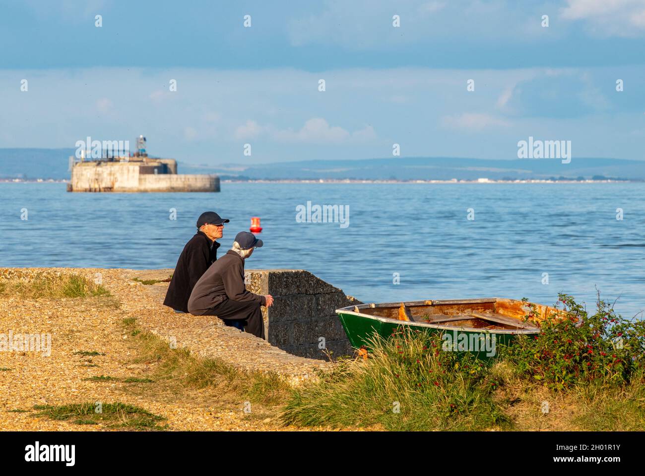 Mann und Frau im Urlaub sitzen an einem sonnigen Herbsttag auf der Insel St. helens duver bembridge von wight mit einem solent-Seefort im Hintergrund. Stockfoto