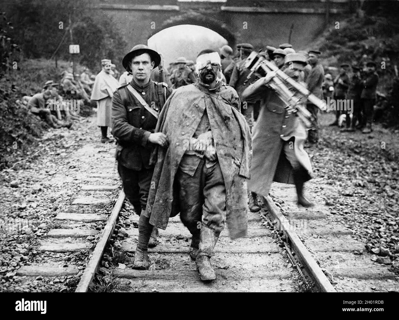 Ein deutscher Gefangener, verwundet und schlammig, unterstützt von einem britischen Soldaten entlang einer Eisenbahnstrecke. Stockfoto