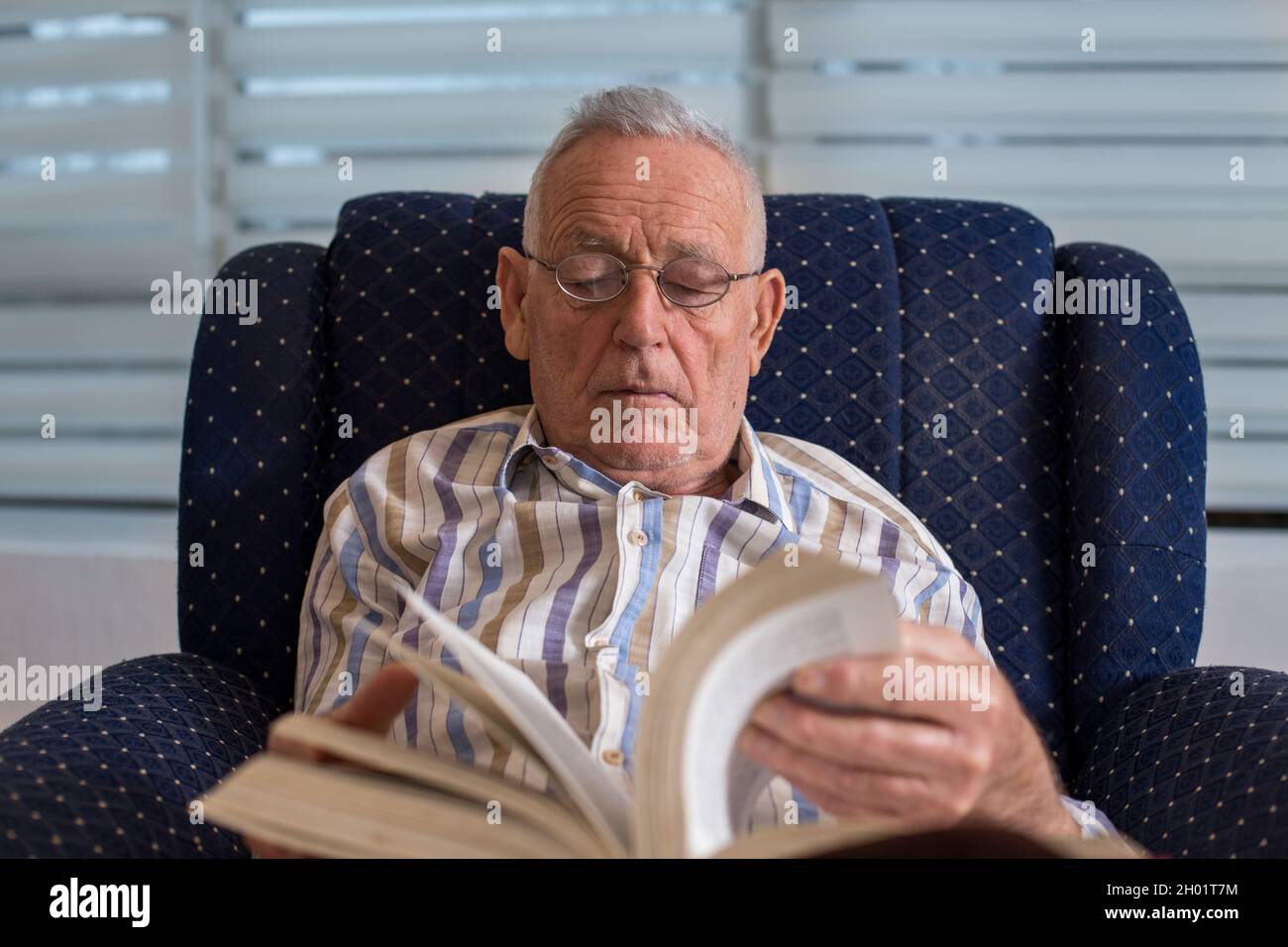 Älterer Mann, der zu Hause im Sessel sitzt und Buch liest Stockfoto