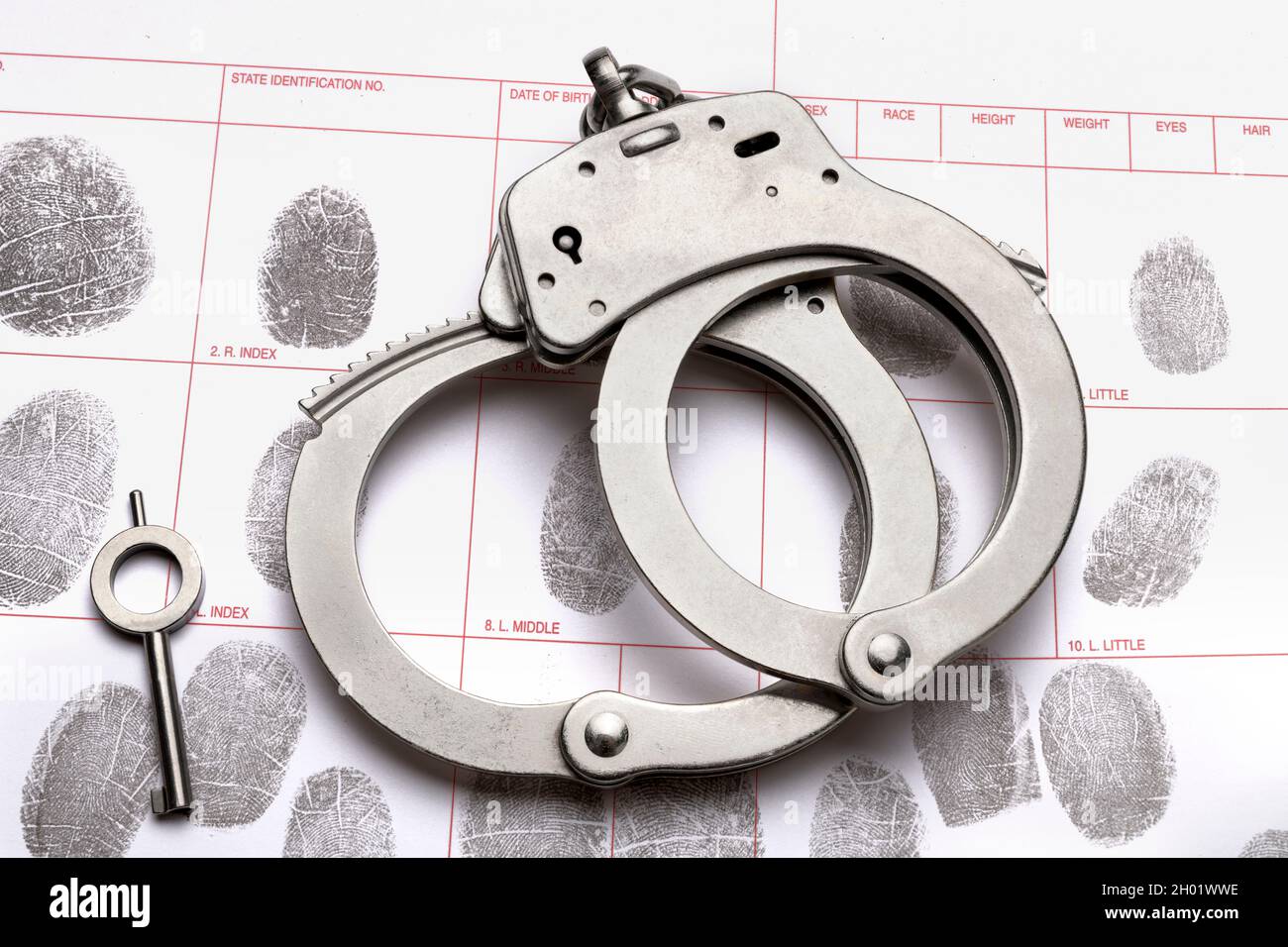 Ein Paar Handschellen und der Schlüssel liegen auf einer Fingerabdruck-ID-Buchungskarte, was auf Kriminalität, Rechenschaftspflicht, Bestrafung und Strafverfolgung schließen lässt. Stockfoto