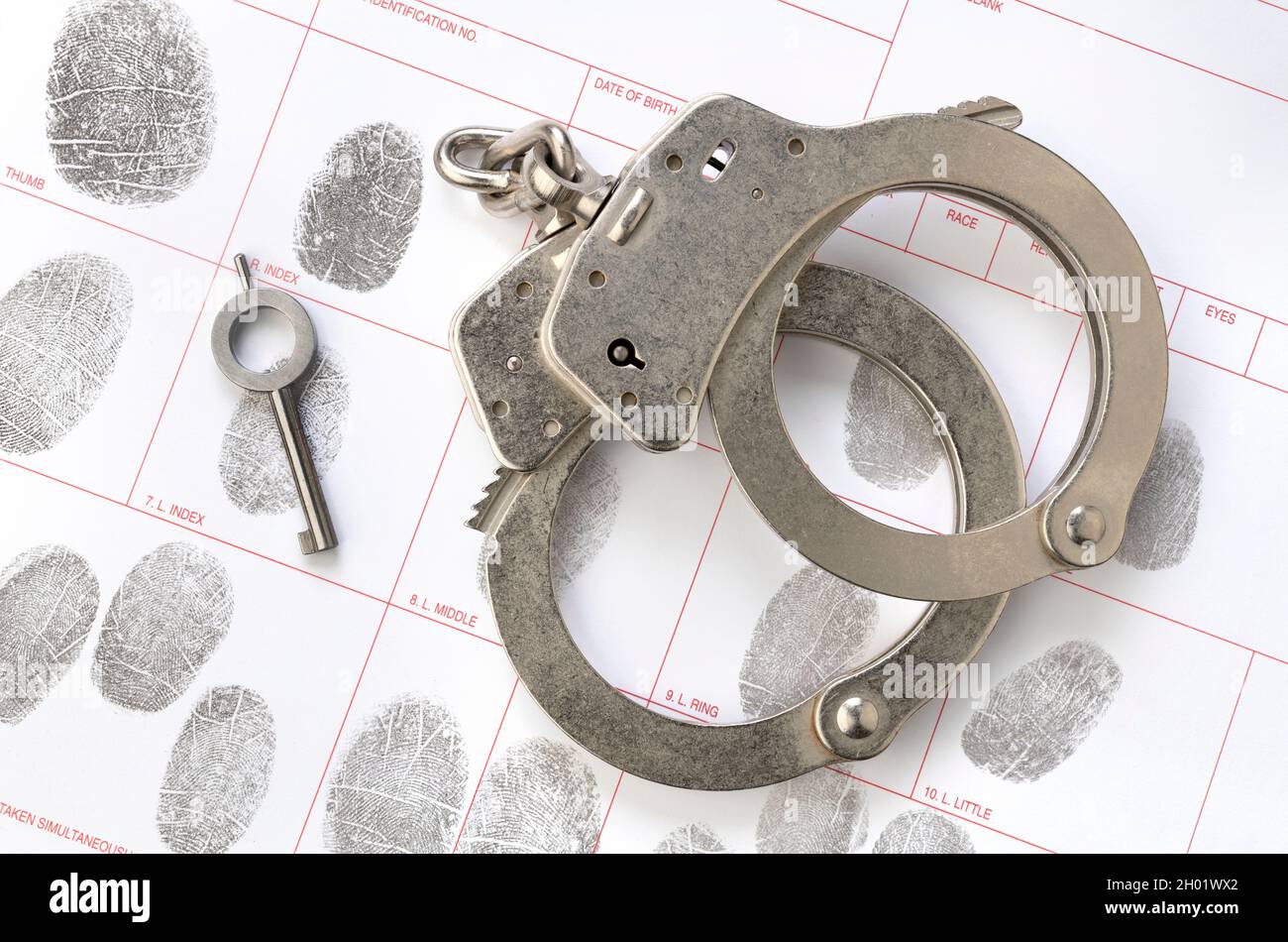 Ein Paar Handschellen und der Schlüssel liegen auf einer Fingerabdruck-ID-Buchungskarte, was auf Kriminalität, Rechenschaftspflicht, Bestrafung und Strafverfolgung schließen lässt. Stockfoto