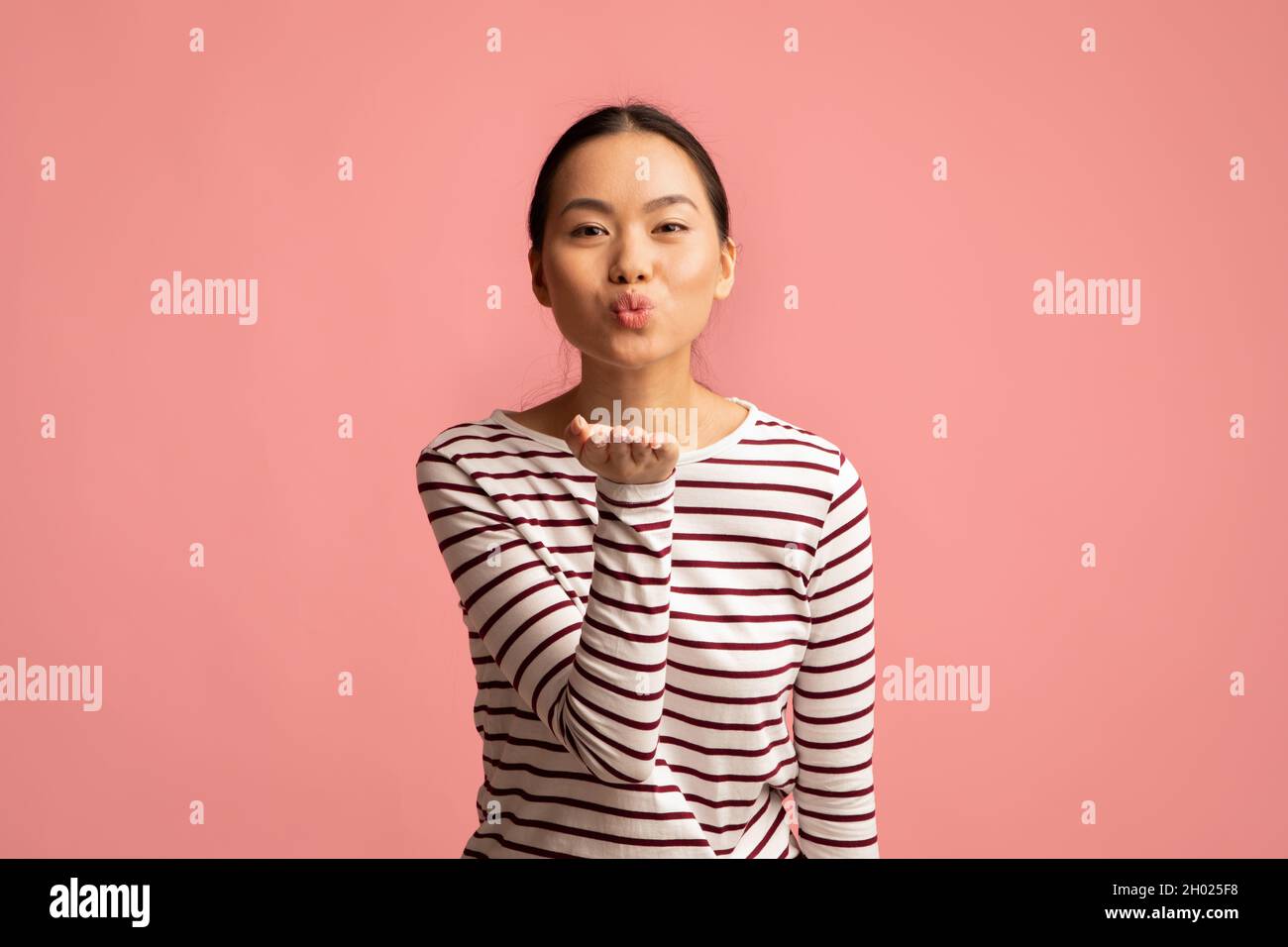 Junge fröhliche asiatische Frau, die Lippen umherschwirrend und Luftkuss an der Kamera bläst, verspielte romantische koreanische Frau, die mit jemandem flirtet, während sie isoliert steht O Stockfoto