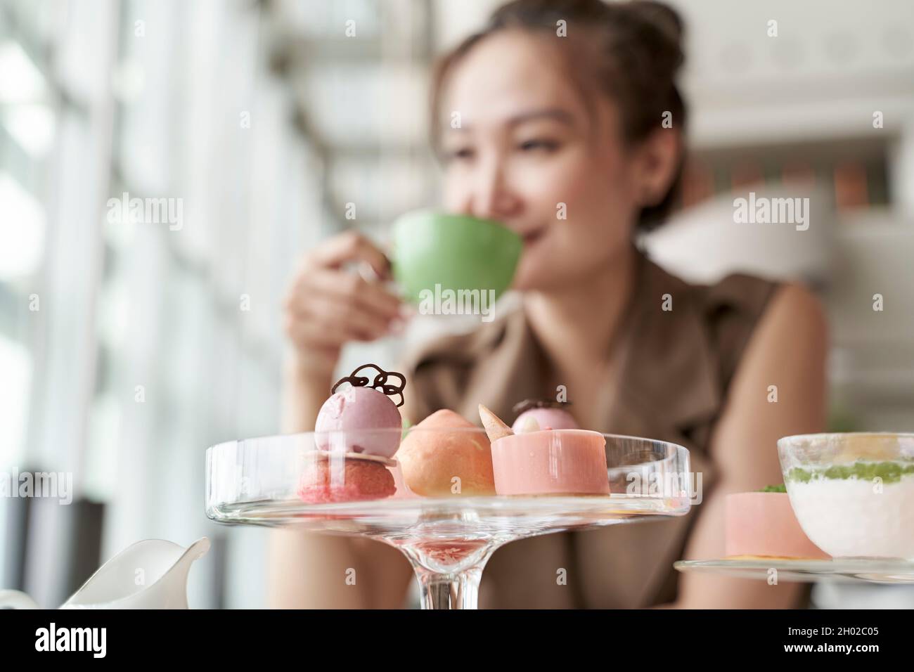 Reife asiatische Frau, die im Café in der Hotellobby am Tisch sitzt und Dessert isst und Tee trinkt Stockfoto
