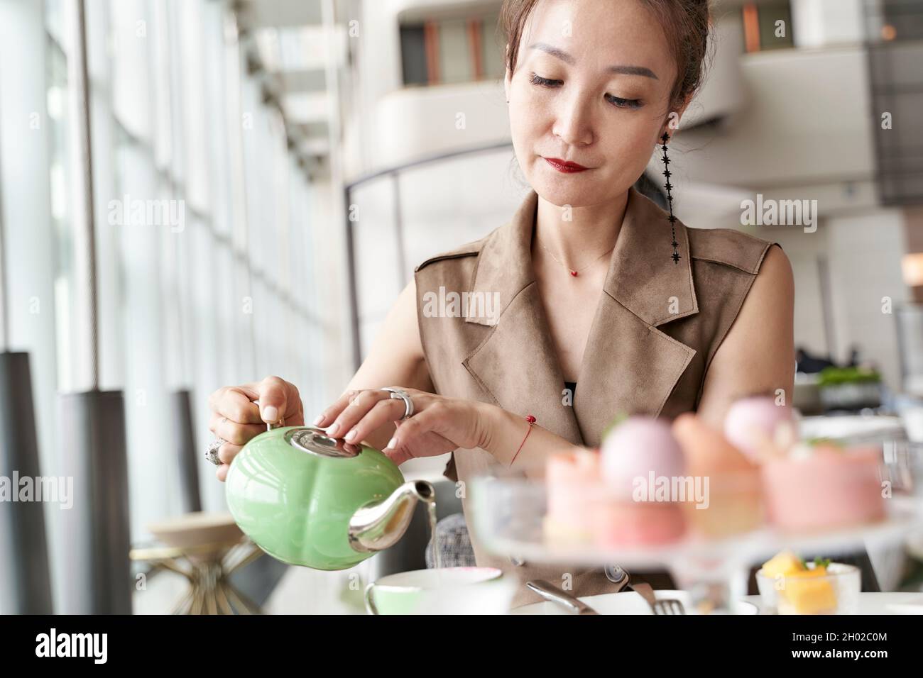 Reife asiatische Frau, die im Café in der Hotellobby am Tisch sitzt und Dessert isst und Tee trinkt Stockfoto