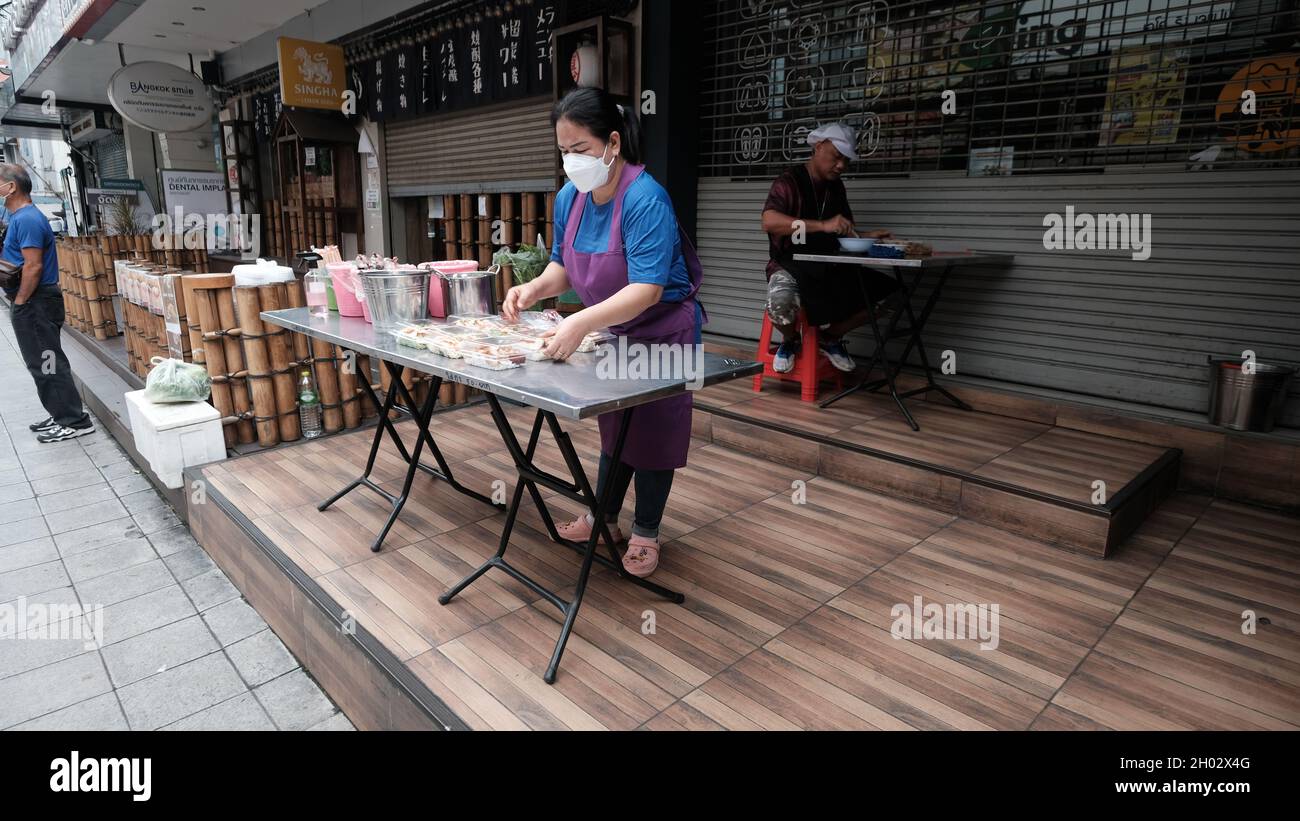 Lady Setting Display und man sitzt essen Street Food am Tisch an der Asoke Road Sukhumvit Soi 21 Bangkok Thailand Stockfoto