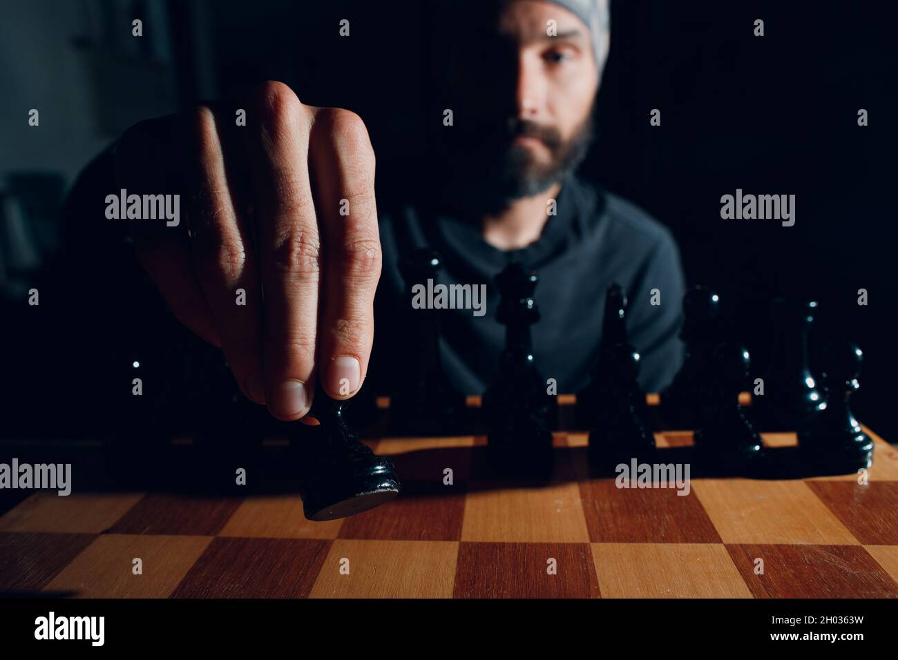 Junger, hübscher Mann, der im Dunkeln ein Schachbrett spielt und seitlich beleuchtet ist. Stockfoto
