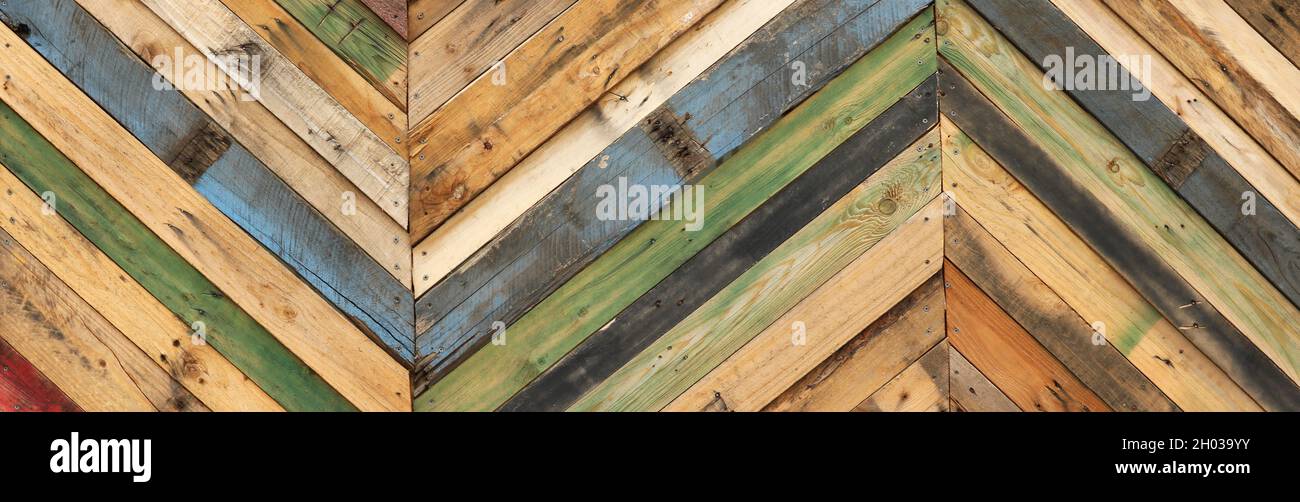 Einzigartige abstrakte geometrische Muster aus recycelten Schnittholzpaletten in diagonalen Streifen. Mehrfarbige texturelle Upcycling-Planken Stockfoto