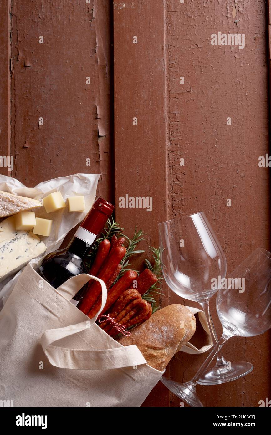 Draufsicht auf Baguette und Flasche Rotwein auf Holztisch mit Weinläsern und Käse Stockfoto