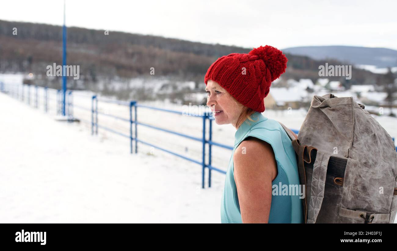 Aktive ältere Frau im Badeanzug mit Rucksack im Winter im Freien, Kalttherapie-Konzept. Stockfoto