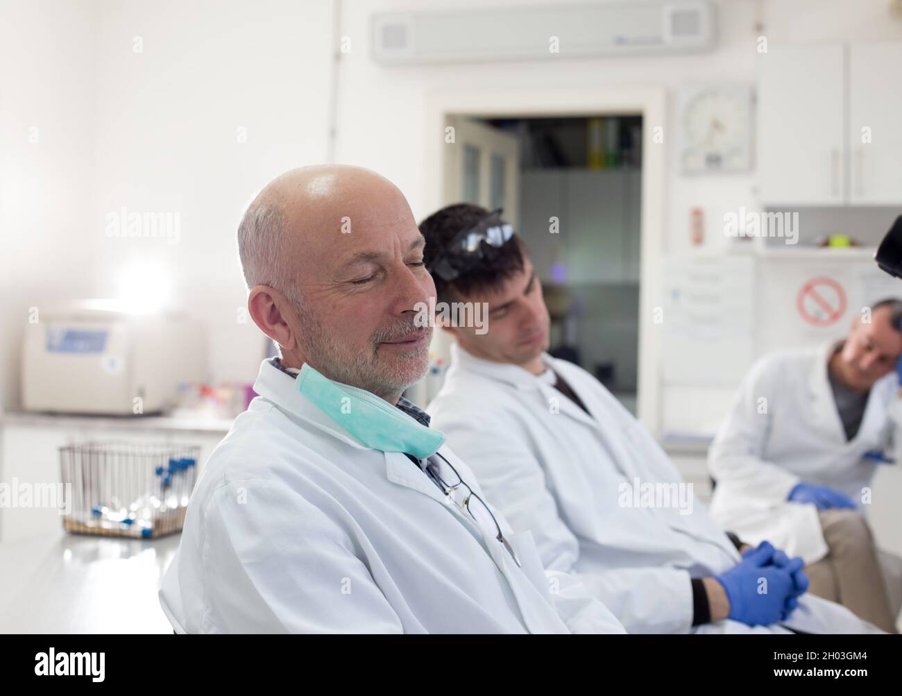 Müde Techniker in weißen Mänteln und mit Handschuhen, die im Labor einschlafen Stockfoto