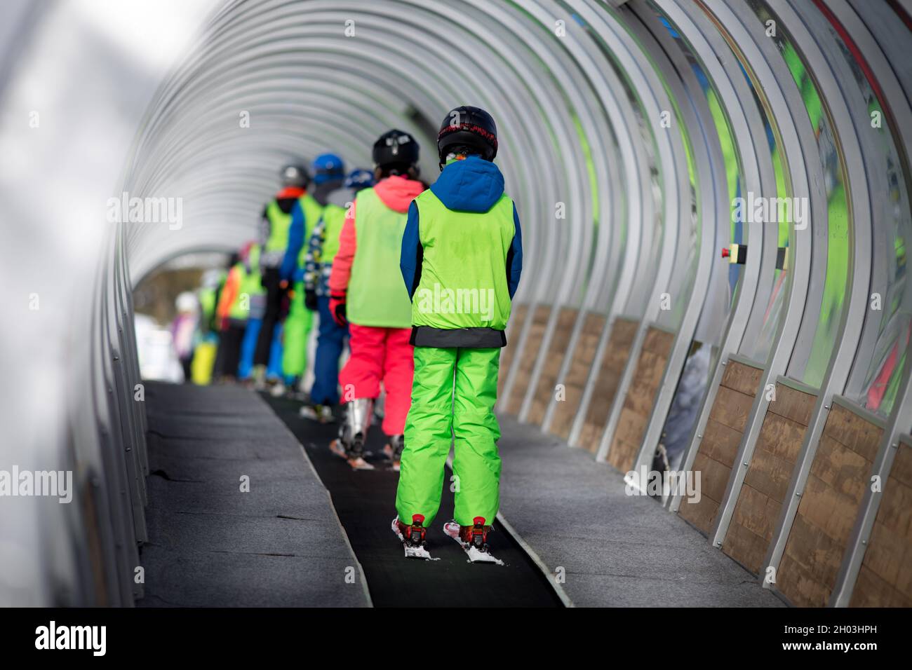 Rückansicht von Kindern in der Skischule beim Heben der Piste mit Förderband im Tunnel Stockfoto