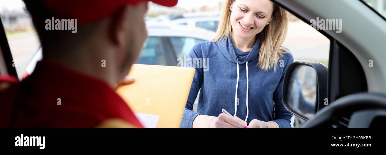 Junge lächelnde Frau, die den Lieferschein in der Nähe des Kurierwagens unterschrieb Stockfoto