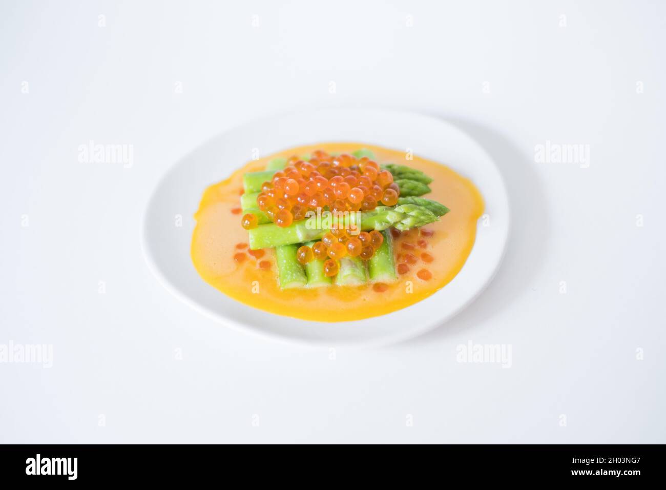 Mini-Spargel mit Sauce und rotem Kaviar auf weißem Teller, isoliert auf weißem, Nahaufnahme, gesunde Ernährung, gesunder Lebensstil, Bild für das Menü Stockfoto