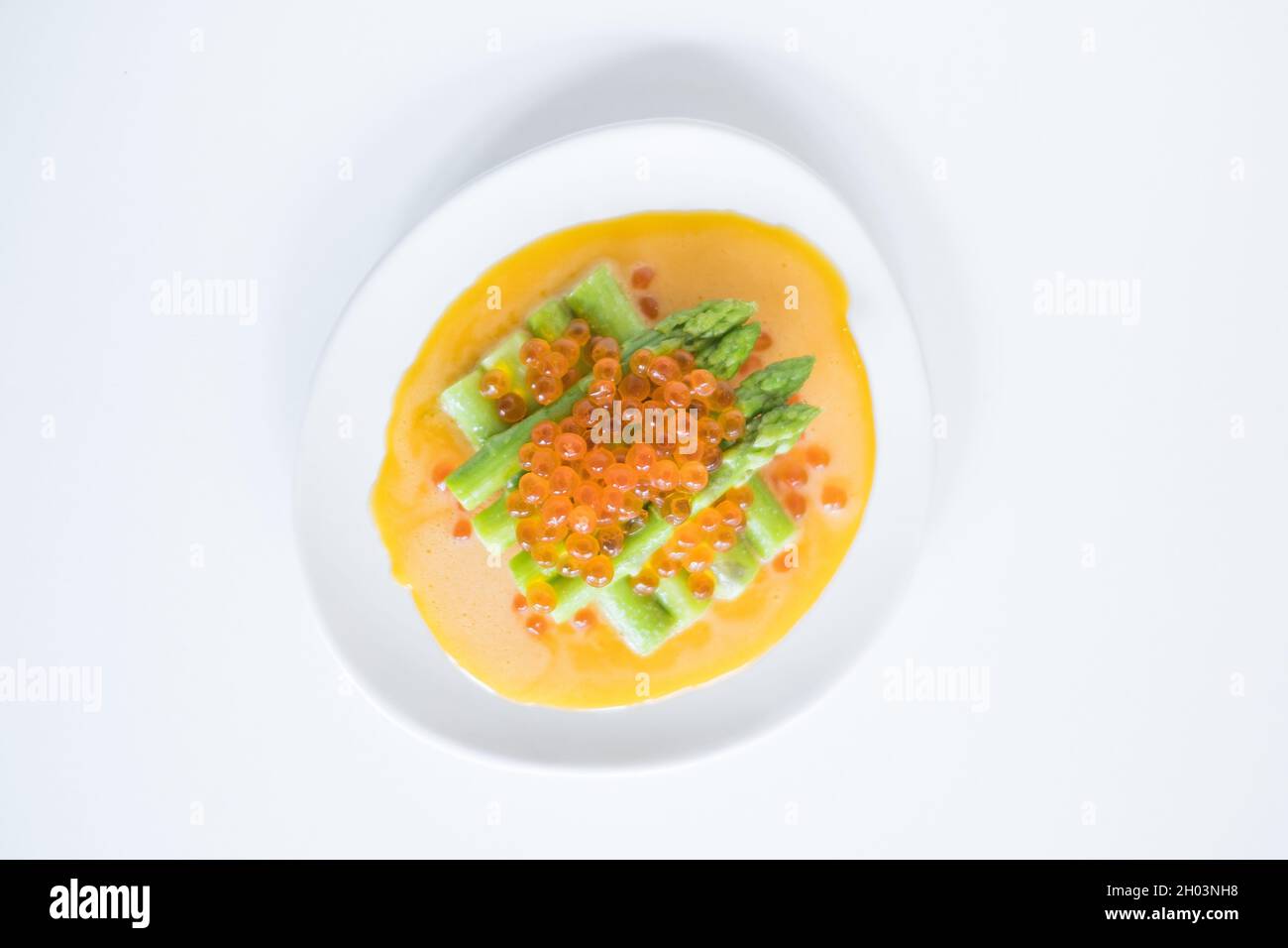 Mini-Spargel mit Sauce und rotem Kaviar auf weißem Teller, isoliert auf weißem, Nahaufnahme, gesunde Ernährung, gesunder Lebensstil, Bild für das Menü Stockfoto