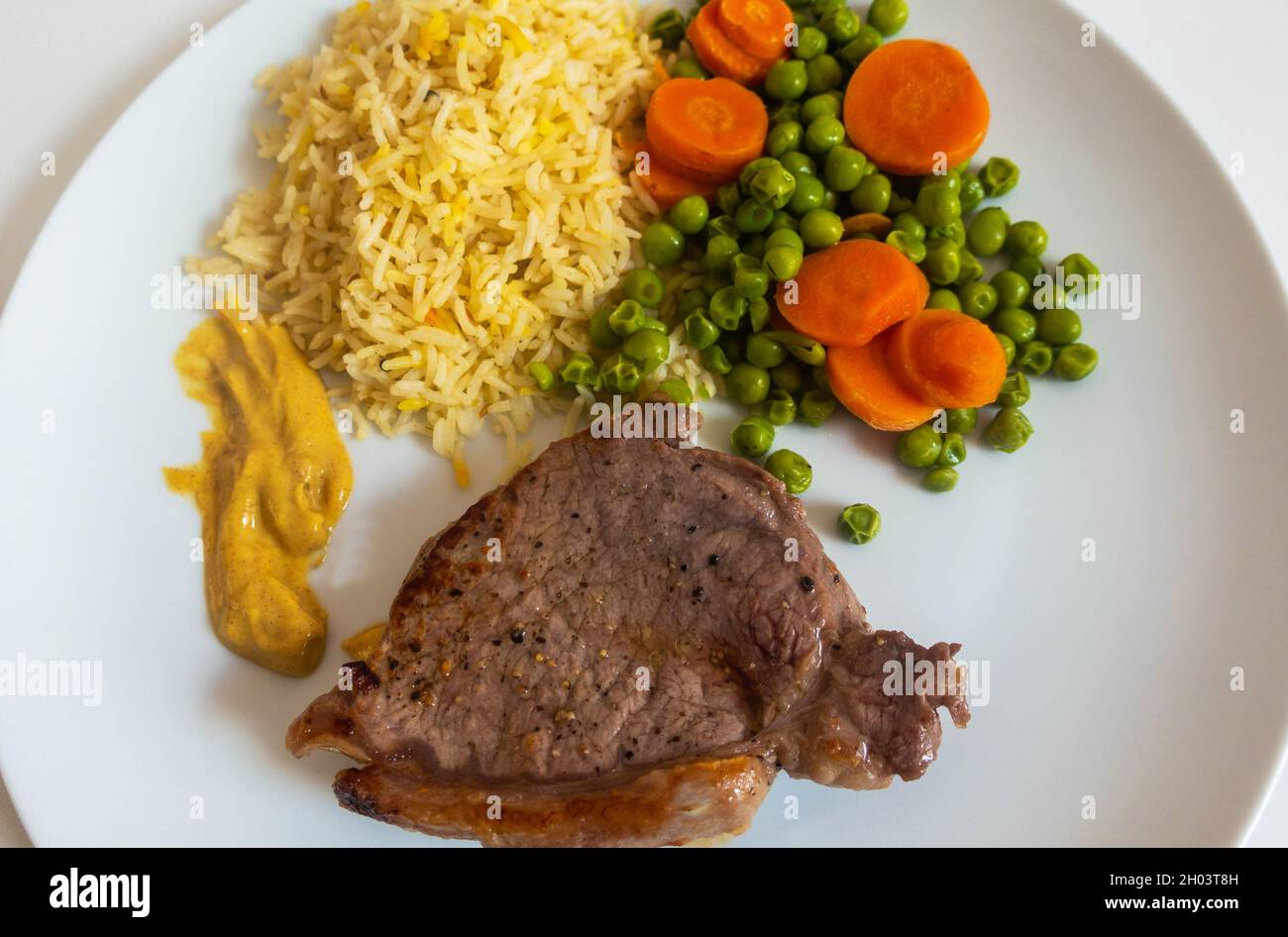 Lendensteak mit Erbsen und Karotten sowie Reis und Dijon-Senf Stockfoto