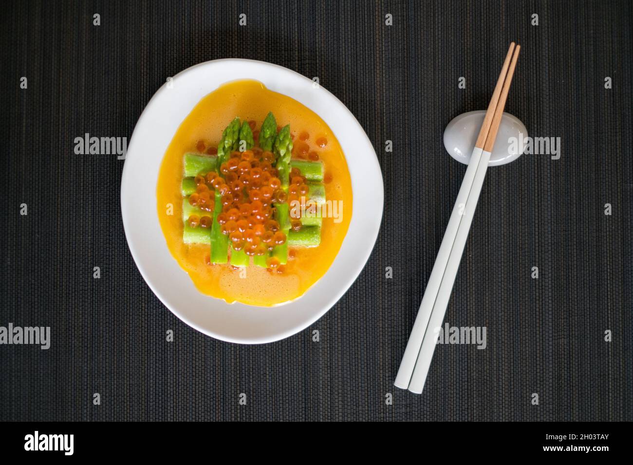 Mini-Spargel mit Sauce und rotem Kaviar auf weißem Teller mit Essstäbchen auf schwarzer Matte im japanischen Restaurant, Nahaufnahme, flaches Lay, Bild für die Speisekarte Stockfoto