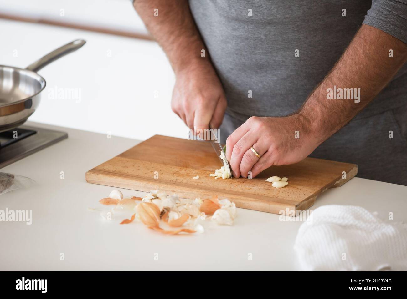 Nahaufnahme eines Mannes, der Knoblauch auf einem Holzbrett in der Küche geschnitten hat Stockfoto