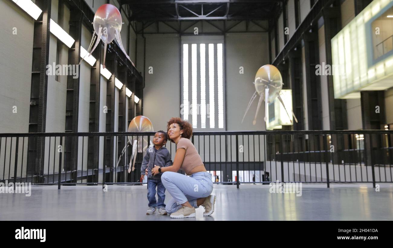 Tate Modern, London, Großbritannien. Oktober 2021. Ein Modell und eine Kinderpose mit der neuen Installation „in Love with the World“, die schwimmende Maschinen namens „Aerobes“ enthält. Die Künstlerin Anicka Yi hat ihr bisher größtes und ambitioniertestes Projekt in der Turbinenhalle der Tate Modern für die renommierte Hyundai-Kommission realisiert. Die Arbeiten werden vom 12. Oktober 2021 bis zum 16. Januar 2022 in der Tate ausgestellt. Kredit: Imageplotter/Alamy Live Nachrichten Stockfoto