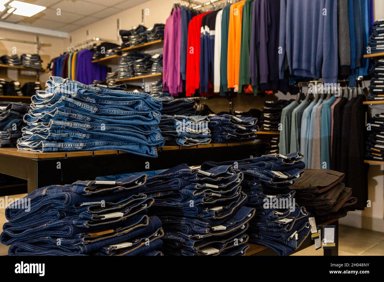 Blaue, blaue Jeans liegen gestapelt im Laden vor dem Hintergrund von Pullovern. Verkauf im Denim-Store. Stockfoto
