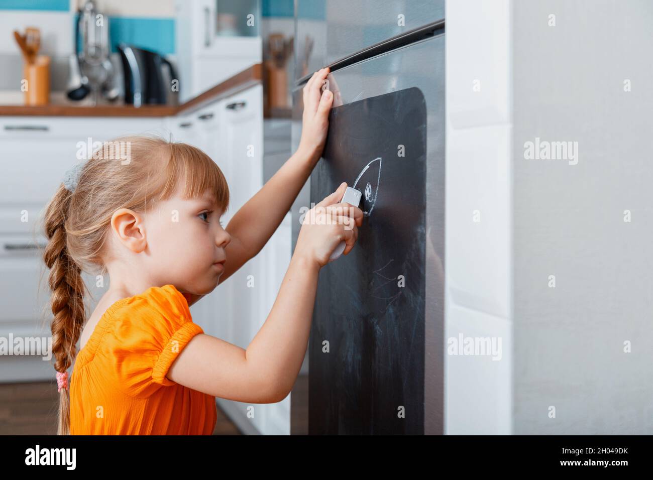Kleine kaukasisch fokussierte Mädchen zeichnen mit Kreide auf Kreidetafel  auf Kühlschrank in der Küche bei gemütlichen Haus Interieur Stockfotografie  - Alamy