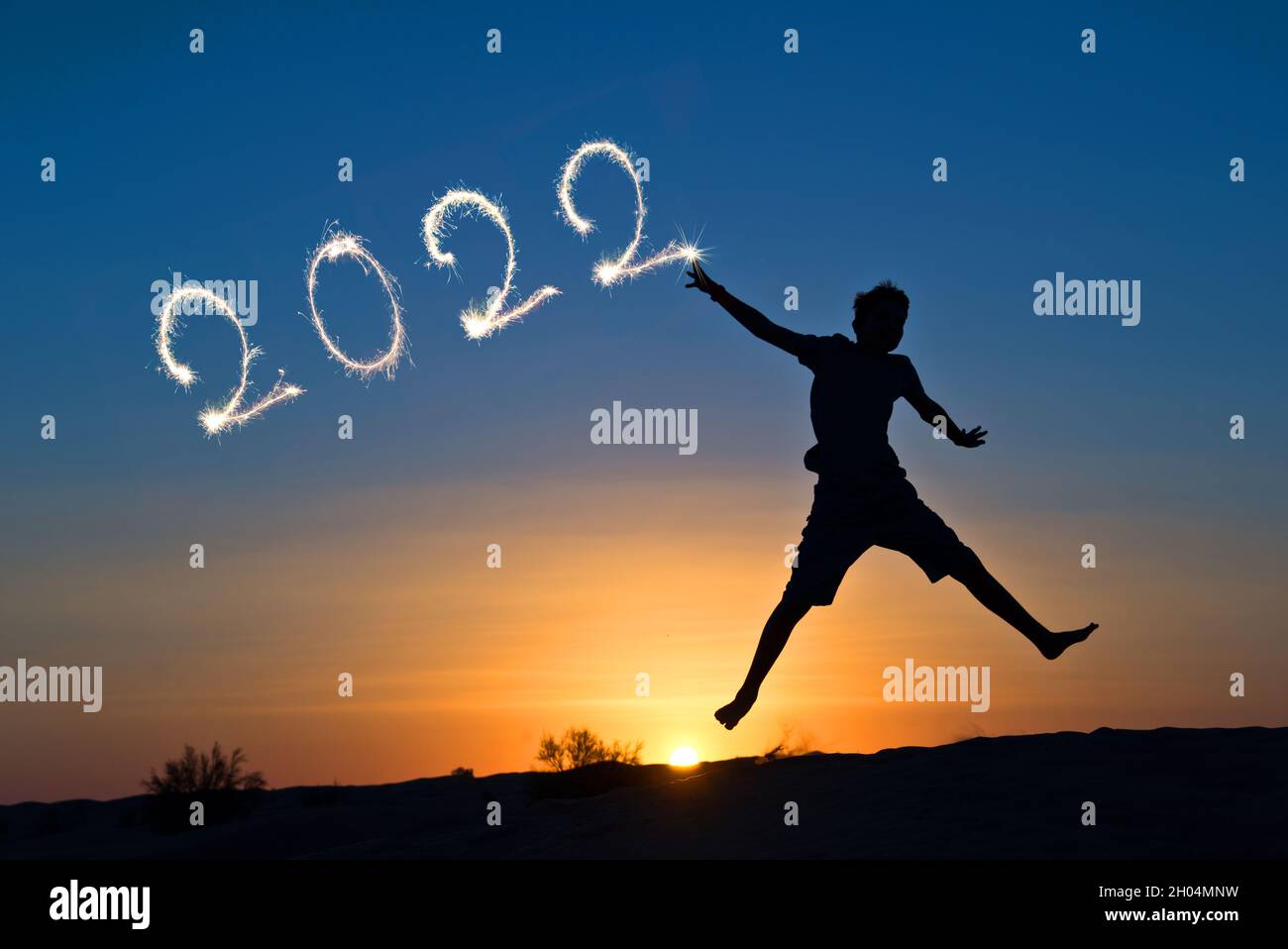 2022 geschrieben mit Funkeln, Silhouette eines Jungen, der in die Sonne springt, Neujahr-Karte Stockfoto